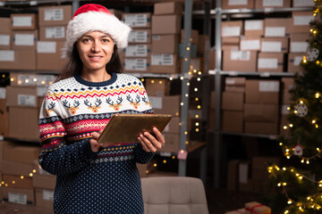 Female warehouse worker wearing Santa hat working at Christmas eve. Christmas sale in e-store.