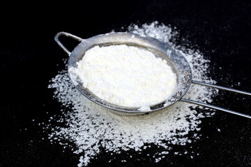 A sieve with white wheat flour lies on a black background.