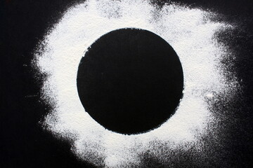 On a black background sprinkled with flour in the form of a circle.