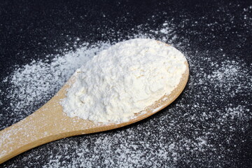 A wooden spoon with flour lies on a black background.