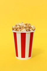 On a yellow background is a striped paper cup with sweet popcorn.