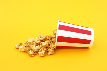 On a yellow background lies a striped paper cup with sweet popcorn.