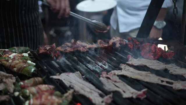 Slow motion shot of a street vendor flipping meats on hsi grill with metal tongs