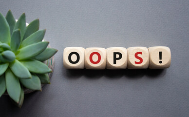 Oops symbol. Concept word Oops on wooden cubes. Beautiful grey background with succulent plant....