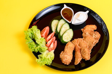 Chicken nuggets with cucumber, tomatoes and lettuce on a black plate, chicken nuggets on a yellow background.