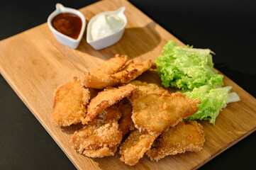 Chicken nuggets with sauces, mayonnaise and ketchup, on a wooden board on a black background and salad leaves.