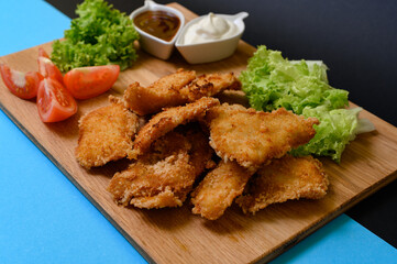 Chicken nuggets with sauces, mayonnaise and ketchup, on a wooden board on a black background and salad leaves.