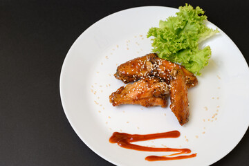 Caramelized chicken wings on a plate with salad and barbecue sauce