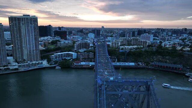 Drone shot of Story Bridge, camera orbiting Howard Smith Wharves with Story bridge in foreground. Citycat boat crossing river. Shot in evening during sunset.