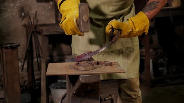 Close-up of a blacksmith man making a metal fence, he knocks with a hammer on hot metal. The process of working in the forge.
