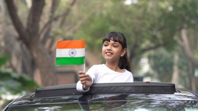 indian little girl exit from car sunroof and waving national flag.