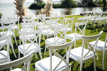 Round arch for a wedding ceremony by the river. White glass chairs stand for guests