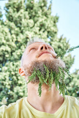 Adult man with fragrant rosemary sprigs in beard and lips. Male looking excited and acting childish with fresh rosemary in sunny meadow - 632448802