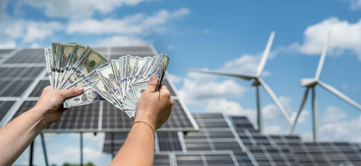 businessman holds dollars as savings after installing solar panels or wind power plants