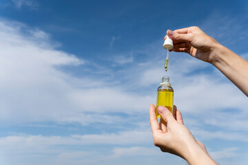 Cosmetic oil with a pipette in female hands on a blue background