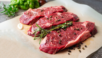 Succulent tender raw lean beef steaks lying on a sheet of oven paper in the kitchen topped with fresh herbs and spices ready to be cooked for dinner