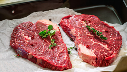 Succulent tender raw lean beef steaks lying on a sheet of oven paper in the kitchen topped with fresh herbs and spices ready to be cooked for dinner