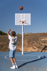 Boy throwing a basketball ball into the hoop while playing on an outdoor court. Sports concept.
