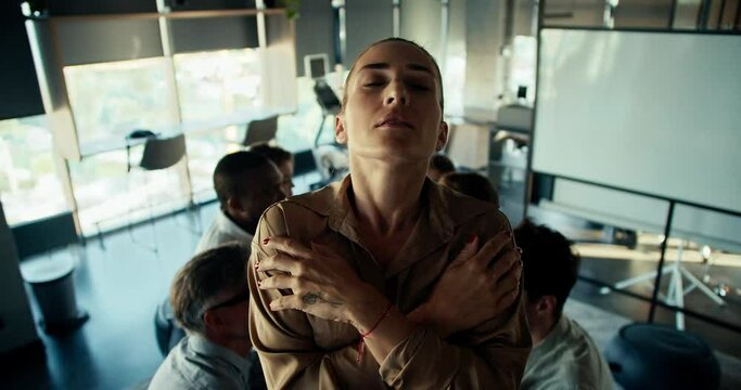 A blonde girl stands on a hill against the background of her colleagues. Trust test, the girl is tense before falling into the arms of her colleagues