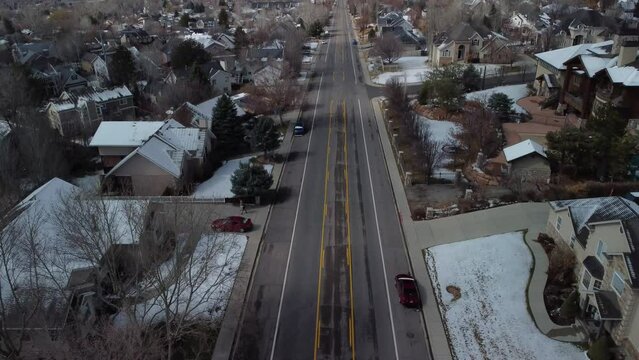 4K Drone footage filmed from above the road over the streets with cars and houses, snowy mountains in the distance, city streets, urban nature, Utah neighborhood, Utah state, SLC, Provo, Orem