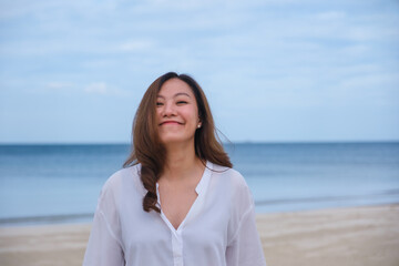 Portrait image of a beautiful young asian woman while strolling on the beach with the sea and blue sky