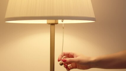 A woman's hand pulls the cord turning on a bedside lamp 