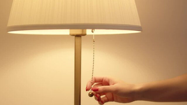 A woman's hand pulls the cord turning on a bedside lamp 