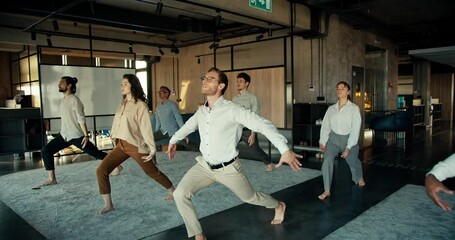 A man in a white shirt and glasses is doing yoga with his colleagues in the office