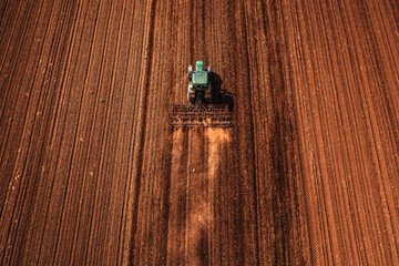 Agricultural tractor with tiller attached performing field tillage before the sowing season, aerial...