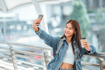 Happy young asian woman taking selfie photo on mobile phone at city, female using smartphone camera...