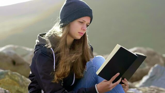 Young woman reading a book while sitting at a rocky beach - slow motion clip 