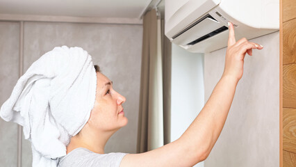 Woman turns on air conditioner in accommodation room. Female person rejoices over repaired electronic device. Keeping temperature in premise