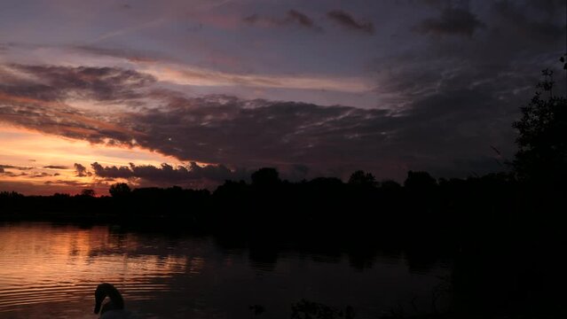Time lapse of sunrise. Dramatic sky with clouds over a lake. Silhouette of a distant forest on the horizon.