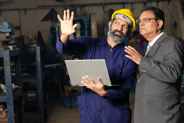 worker using laptop while discussing with factory owner