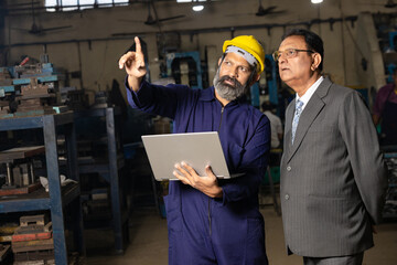 worker using laptop while discussing with factory owner