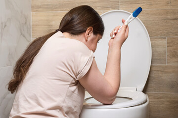 Expectant mother vomits sitting near light toilet bowl in bathroom. Toxicosis in pregnant female...