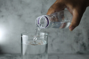 pouring water from bottle into glass on grey and texture background