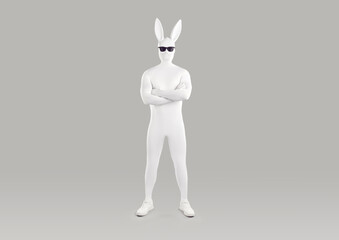 Full length portrait of faceless unrecognizable person in white spandex costume, hare mask with long ears and black glasses. Incognito funny man in bodysuit with crossed arms on grey background.