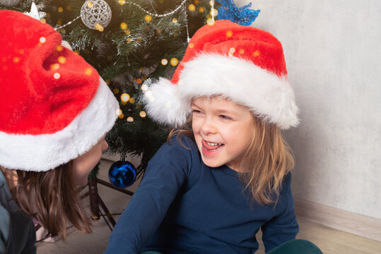 Happy cheerful children in santa hats under the Christmas tree. Christmas holiday. Real people, simple life.