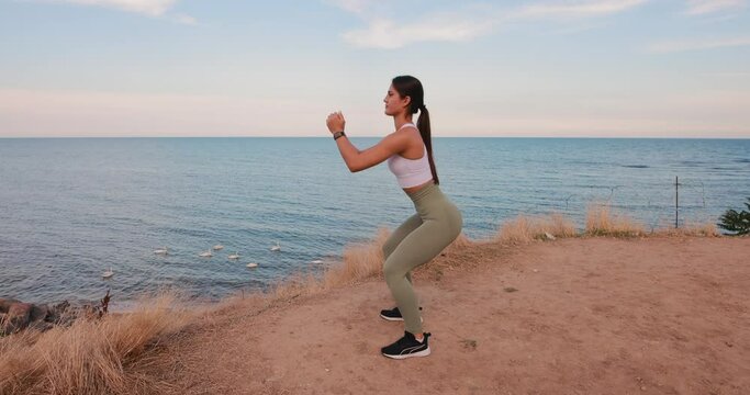 Woman in sport clothes squats at the sea