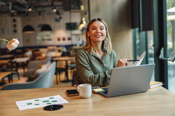 Woman analyst working with documents and use laptop while sitting in cozy coworking near window