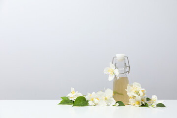Jasmine flowers and glass bottle on gray background, space for text