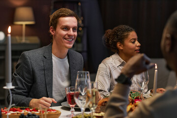 Happy young man looking at his buddy during conversation by festive dinner while sitting in front of him by served table at home party