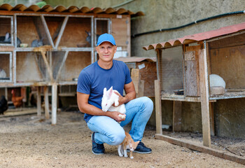 Farmer caucasian rural portrait in countryside with white rabbit in his arms outdoors outside.