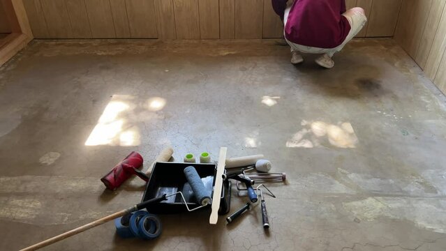 Painting doing home improvement diy remodel of basement with light wood panels and concrete floor painting bright white husband and wife team couple working together. Wide angle of setup and prep.