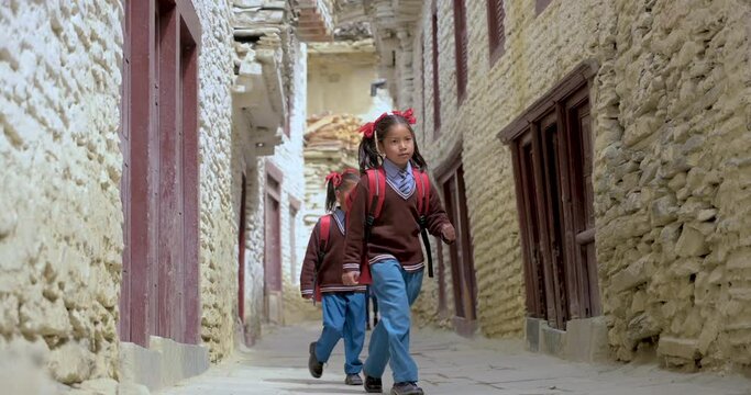 Nepali kids going their school in Village of Mustang Nepal. Wearing their tidy uniforms and carrying bags they walk on the alley of Mustang. Happy kids and morning time sun. 4K