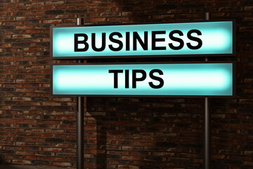 Obraz premium Business tips. Black letters on a blue illumintaed light box, red brick wall. Advice, guideline, rule, strategy, hint, instruction, procedure, control, organization. 3D illustration