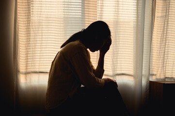 Silhouette photo of young Asian woman feeling upset, sad, unhappy or disappoint crying lonely in her room. Young people mental health care problem lifestyle concept.	 - Powered by Adobe