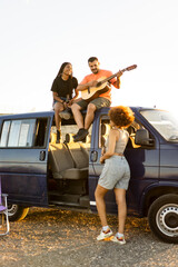 Vertical photo of 3 multiethnic young people having fun camping with a motorhome in the middle of...