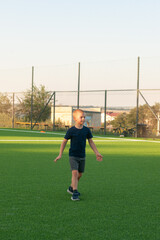 The boy is on the football field waiting for training. Wearing a blue t-shirt and black shorts